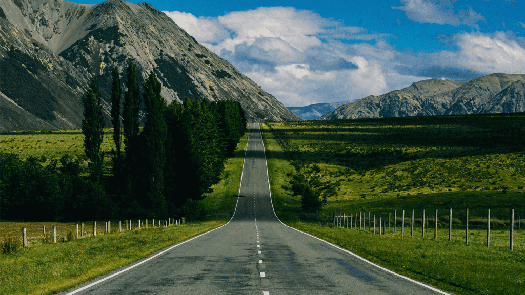 An empty road running through green farmland towards a mountain range