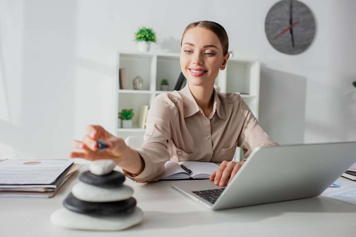 A woman working at a desk with a laptop and a stack of balancing stones