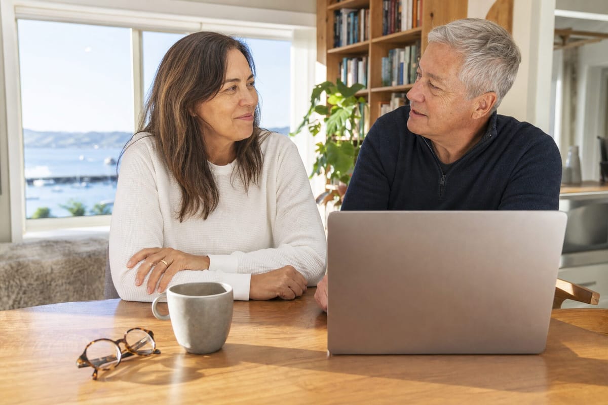 A couple in their fifties talking at a sunlit dining table in a New Zealand home