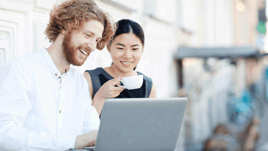 Two colleagues smiling at a laptop together over coffee