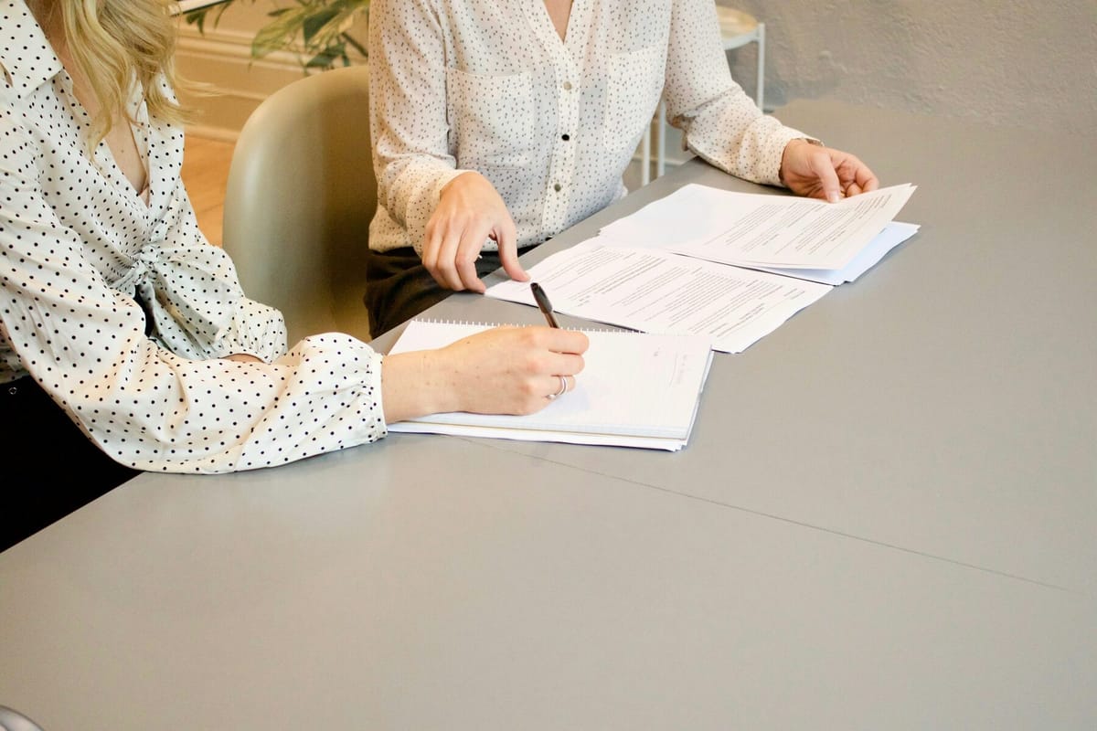 Two people working through a stack of documents together at a desk, one signing.