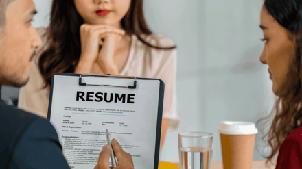 A resume on a clipboard on the table between three people in a meeting