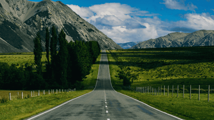 An empty road running through green farmland towards a mountain range