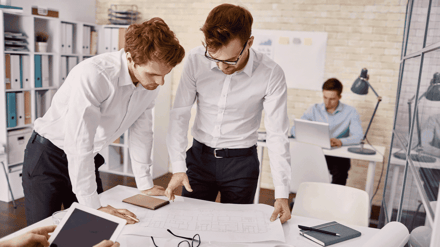 Two colleagues leaning over an office desk looking at a plan