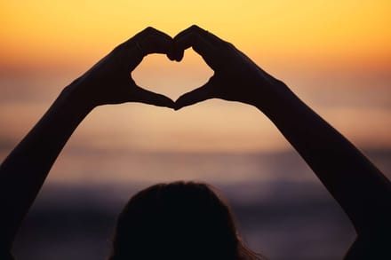 Two hands forming a heart shape against a sunset