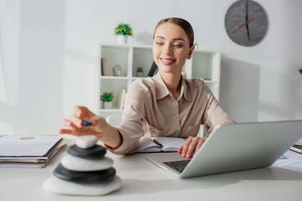 A woman working at a desk with a laptop and a stack of balancing stones