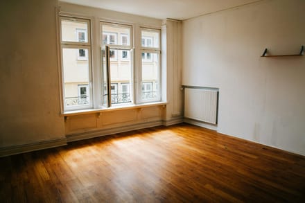 An empty room with bare wooden floorboards and a tall window