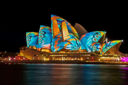 The Sydney Opera House lit up at night with colour projected across its sails