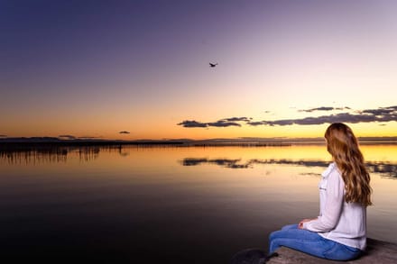 A person sitting alone at the edge of a lake at sunset