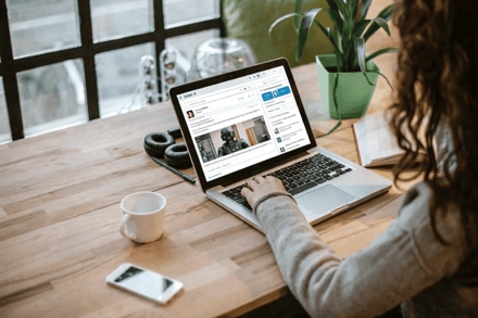 Someone at a laptop scrolling a professional network feed, coffee beside it