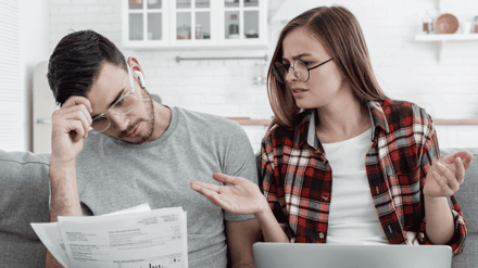 A couple at a table looking puzzled over paperwork