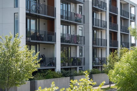 A low-rise purpose-built rental apartment building in a New Zealand city on a bright morning, bicycles and planters on the balconies