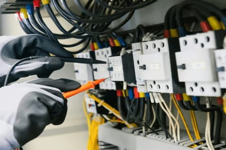An electrician testing an electrical panel with a multimeter, one of the licensed trades the Green List is built around.