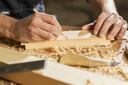 A carpenter marking a length of timber with a pencil, wood shavings and chisels on the bench