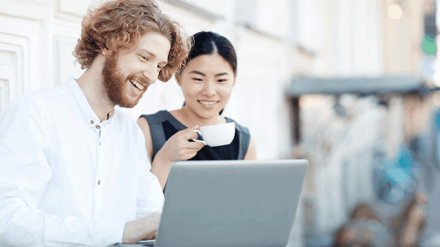 Two colleagues smiling at a laptop together over coffee