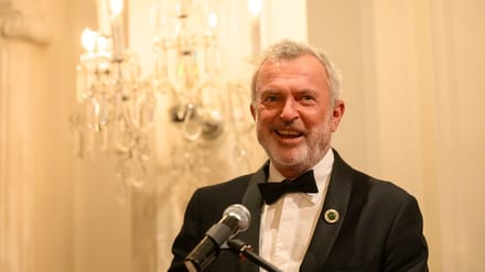 Sam Neill smiling at a formal event, warm and at ease.