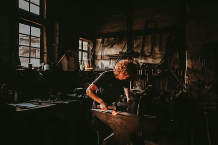 A blacksmith shaping hot iron at an anvil, working a specialised trade by hand.