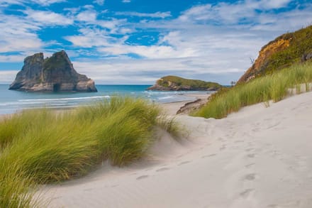 Dunes and marram grass leading down to a beach with rock arches offshore