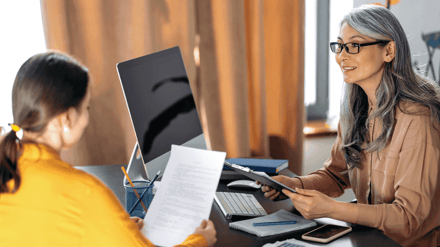 Two women at a desk reviewing a printed document together