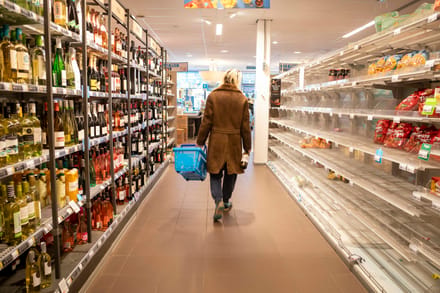 A shopper walking down a supermarket aisle with a basket