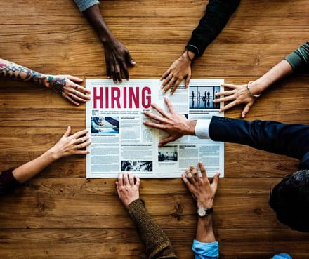 Several pairs of hands over a newspaper with a hiring headline