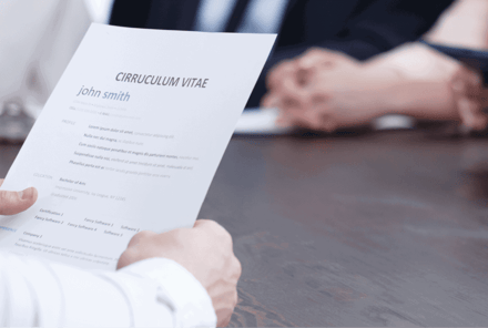Someone holding out a printed curriculum vitae across a desk