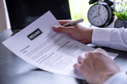 Hands reviewing a resume at a desk beside a clock
