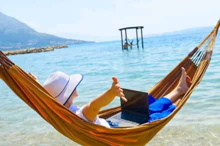 Someone lying in a hammock with a laptop, beside a turquoise sea